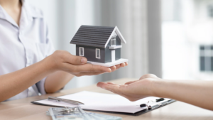 Person holding a model home in their hands with another hand ready to catch it, symbolizing the layers of protection needed for home security.
